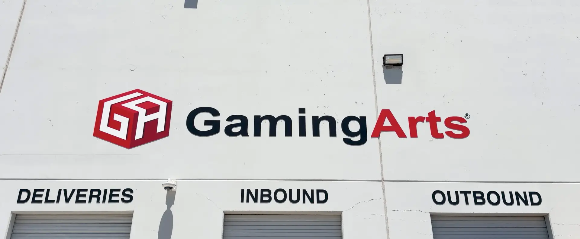 The exterior wall of a building, home to the renowned gaming technology provider Gaming Arts, displays its logo and name above three labeled loading doors: Deliveries, Inbound, and Outbound.
