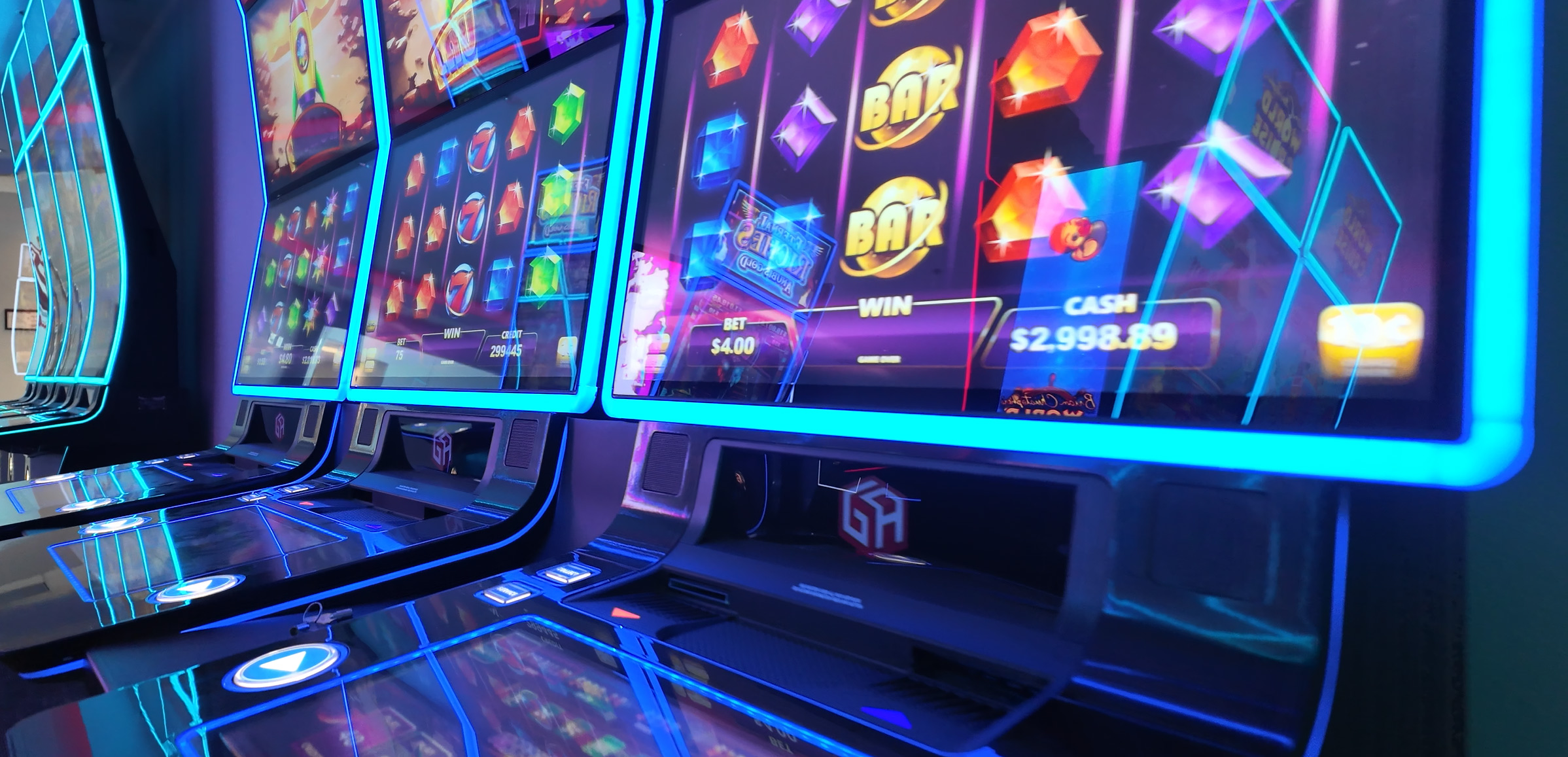 Close-up of brightly lit slot machines in a casino, with colorful graphics on the screens showing symbols, winnings, and a cash amount of $2,998.89. The sleek cabinets feature blue neon lights and touchscreen controls, adding to the vibrant atmosphere.