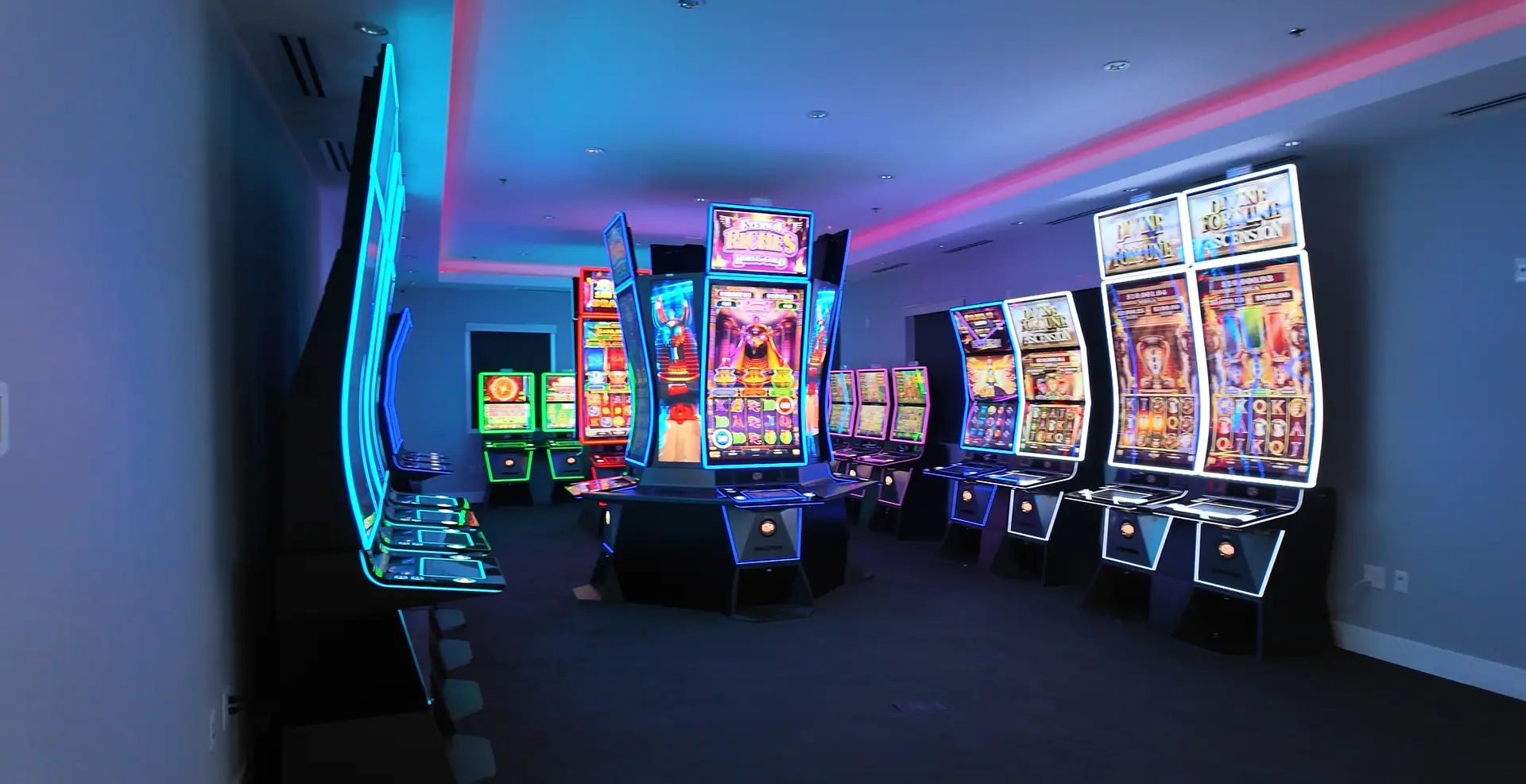A row of brightly lit slot machines lines the walls of a modern, empty casino room. The machines display various colorful graphics, and the space is illuminated by neon lights—a vibrant environment where casino gaming careers come to life behind the scenes.