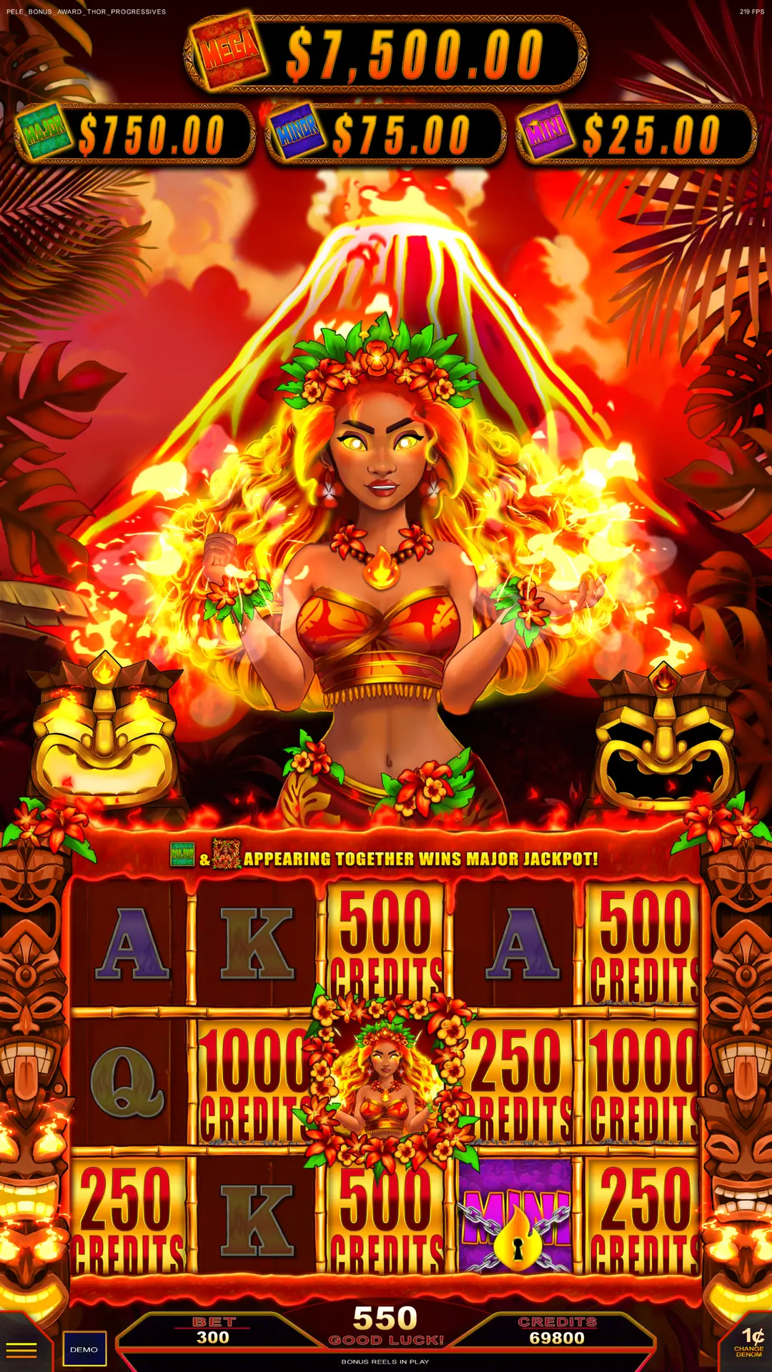 A vibrant slot machine screen features a fiery goddess with glowing hands, surrounded by flames, a volcano, tiki masks, and tropical plants. Bright jackpot amounts are displayed at the top.